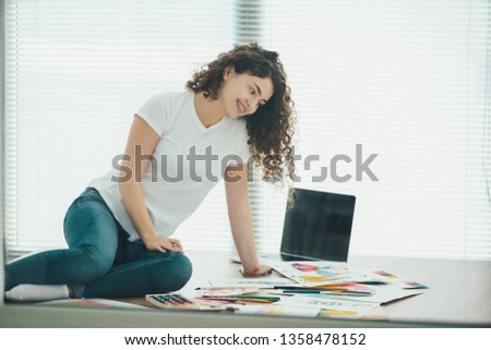 The curly girl sitting on the table and drawing on the paper