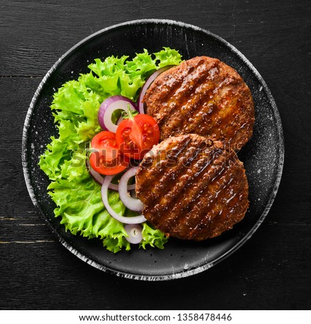 fried cutlet for burger with vegetables. In a black plate on a wooden background Top view. Free space for your text. Flat lay