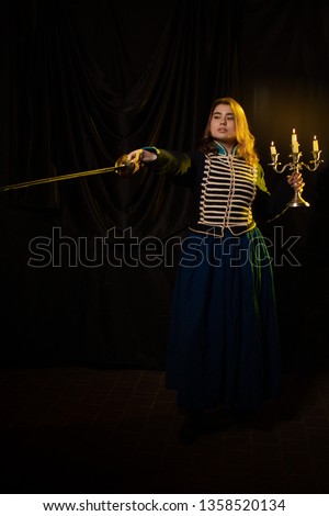 A girl in a hussar's uniform with 19th century epaulets in yellow light against a dark background