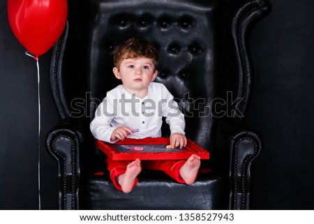 Little boy sitting on the armchair with red framed picture on the St. Valentine's day. Black background and mother's woman day concept.