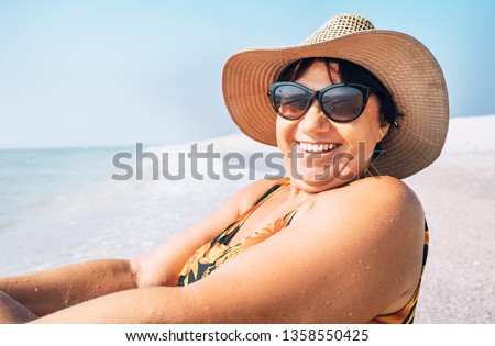 Happy smiling senior woman in sunglasses and big hat taking sun bath on the seaside portrait Royalty-Free Stock Photo #1358550425