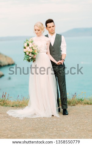 Stunning bride and groom hug each other tender standing on the golden hill near sea