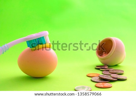 Toothbrush with toothpaste is on the whole egg. A symbol of the strength of the teeth. Oral hygiene. Next to the barrel scattered metal money - coins, cents. Healthy teeth concept. Green background.
