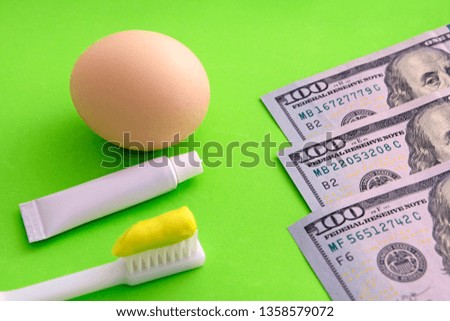 Toothbrush and tube of toothpaste next to a brown egg on a green background. Dollar bill. Egg as a symbol of the strength of human teeth. Expensive dental services.