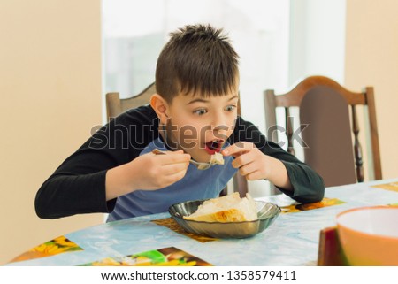 boy of European appearance sits at the table and has breakfast, he eats dairy products with a fork and makes emotions. Food concept
