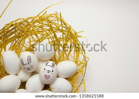 White chiken eggs with pictured rabbits in nest on white background. Preparing for Easter celebrating. Easter concept.