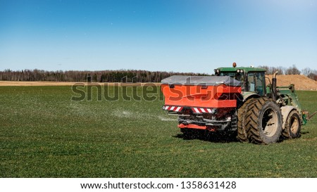 Tractor fertilizing in field on a sunny day with blue sky background.