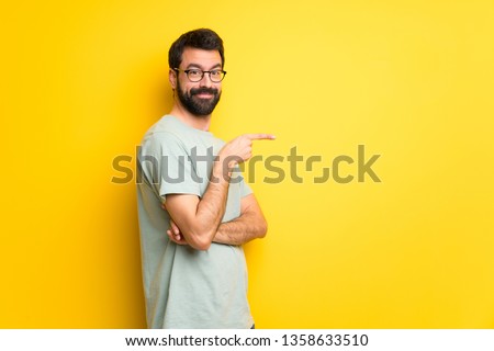 Man with beard and green shirt pointing finger to the side in lateral position