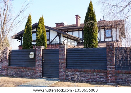 brown fence of wooden planks and bricks with a closed door and green coniferous trees