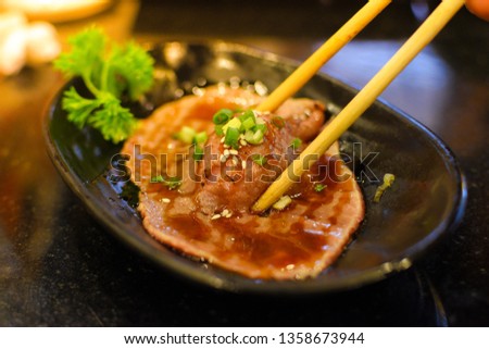 Photography of chopstick clamping medium rare grill pork sushi for eat with Fresh vegetable and sesame. Japanese food serve with vegetable on pottery dish.