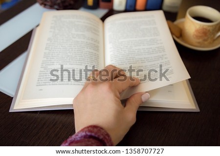 detail of female hand turning a page of book on dark wooden tabl