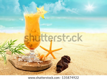Colourful carambola and orange cocktail ina tall glass served on a wooden board on a golden beach at a tropical holiday resort during an enjoyable summer vacation