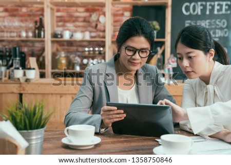 right beautiful asian female manager helping new female employee giving advice sitting in cafe bar working. two office co workers sitting in coffee shop working on digital tablet smiling teamwork.
