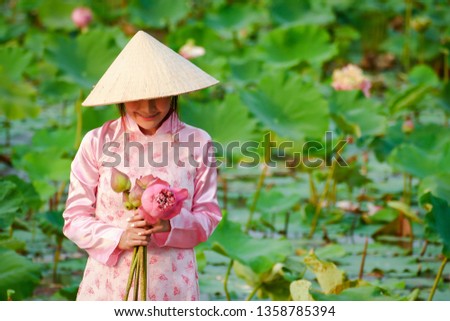 Vietnamese girl wearing a hat, wearing a pink dress, holding a lotus flower in a large lotus pond.
