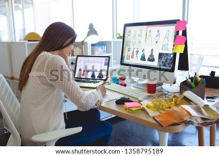 Side view of young Caucasian female fashion designer working at desk in a modern office 