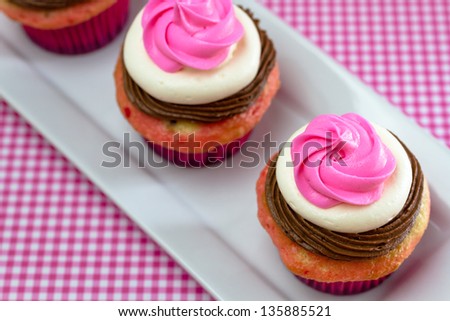 Line of 3 neapolitan frosted cupcakes on long white plate with pink gingham checked tablecloth