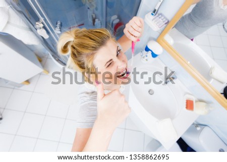 Woman brushing cleaning teeth closeup. Funny blonde girl with toothbrush in bathroom making thumb up hand sign gesture. Oral hygiene. Unusual wide angle top view
