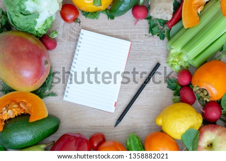 Vegetables and fruits closeup on wooden background. Mango, radish, yellow pepper, red pepper, lemon, cucumber, dill, tangerine, parsley. In the middle of the cutting Board and a notebook with a pencil