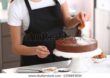 Young female confectioner decorating cake in kitchen