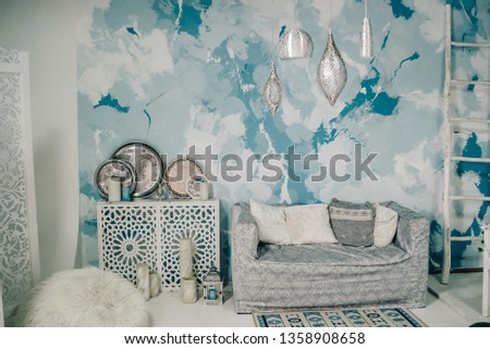 photo studio with white sofa, white bedside table, aluminum decorative plates, designer chandelier against the background of the blue wall
