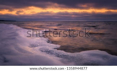 colorful picture of ice and snow on a beach in the foreground, clouds and a streak of light in the background