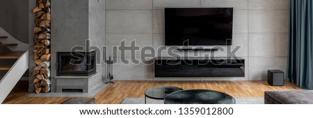 Tv living room with cement wall and wall mounted fireplace, panorama Royalty-Free Stock Photo #1359012800