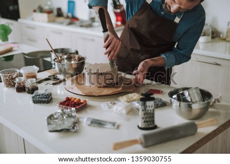 Close up of the concentrated confectioner standing with cake icing spreader in his hand and touching the wooden board under the cake
