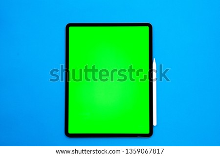 new tablet on a Blue background with a keyboard and pen, and green screen