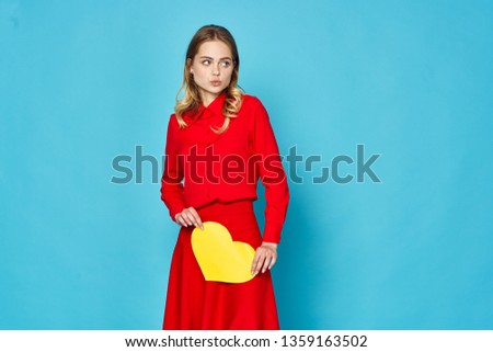 A woman in a red dress with a yellow heart made of paper in her hands a blue background