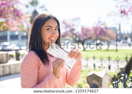 Positive pretty Indian girl showing airline ticket while looking at camera. Smiling young woman getting ready for vacation. Tourist concept