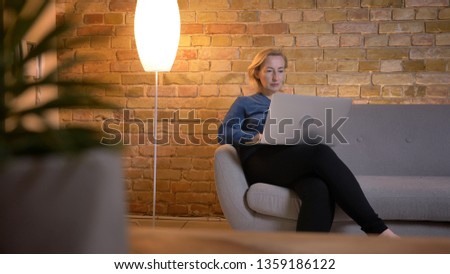 Portrait in profile of senior caucasian woman sitting on sofa and working with laptop attentively in cozy home atmosphere.