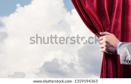 Human hand opens red velvet curtain on blue sky background