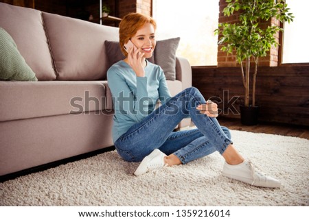 Close up photo amazing beautiful she her lady hand hold telephone ear tell say chatting wear blue pullover jeans denim clothes sit floor fluffy carpet divan sofa couch house loft living room indoors