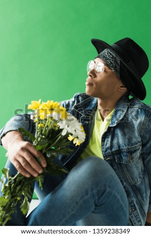 stylish mixed race man in denim posing with flowers on green screen