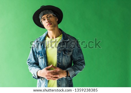 stylish mixed race man looking at camera and posing on green screen