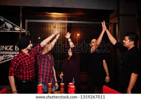  Group of indian friends having fun and rest at night club, drinking cocktails and giving high five together.