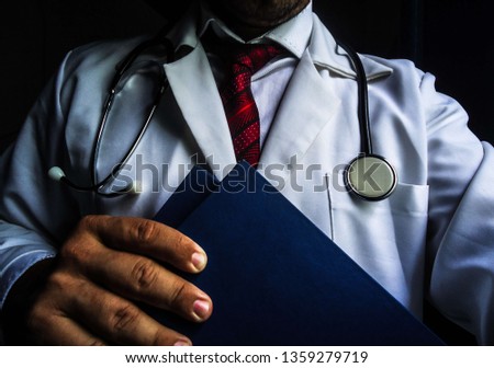Young man wearing medical clothes, with red tie and holding books. With a stethoscope around the neck. This image can be used in subjects related to medicine. April 2019 image. Royalty-Free Stock Photo #1359279719