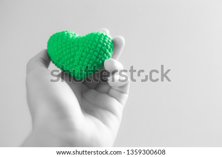 Hand holding green heart with gray background. Selective focus