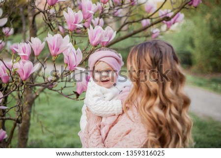 Beautiful young mother and little daughter near the magnolia. Spring family portrait. Blooming tree.