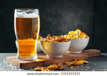 Glass of lager beer with snack bowls on dark stone background Royalty-Free Stock Photo #1359323333