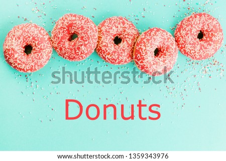 Five coral donuts lying in a line. Donuts decorated with icing on blue background. Top view with text donuts.