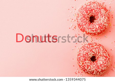 Two coral donuts lying in a line. Donuts decorated with icing on pink background with text Donuts. Top view.