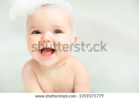 A Baby girl bathes in a bath with foam and soap bubbles Royalty-Free Stock Photo #1359375779
