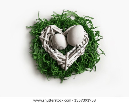 White Easter eggs on green artificial grass and a worn heart of wooden white rods. Minimalistic background for postcards.