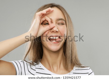 lifestyle, body language, emotion and people concept: Close up portrait of beautiful joyful female smiling, demonstrating white teeth, looking at the camera through fingers in okay gesture. 