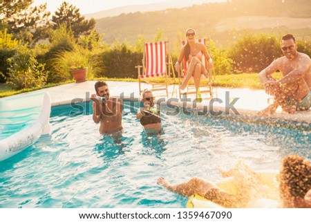 Group of friends at a poolside summer party, having fun in the swimming pool, drinking beer and splashing water