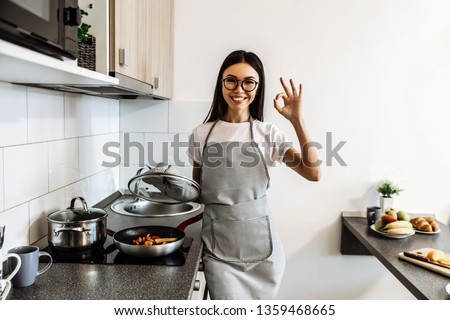 Cooking. At home. Asian girl is showing Ok sign and smiling; in the kitchen