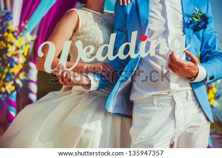 Wedding couple holding a inscription made of wood with the word "wedding"...