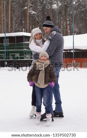 A little girl with his parents skates on the outdoor ice rink in the winter. Active family sport, winter holidays, sports clubs