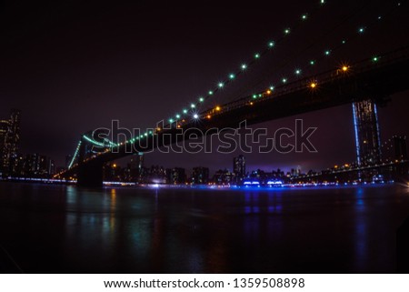New York City skyline as seen from Dumbo Brooklyn, colorful sky and bridge. Reflection on the Hudson River water.